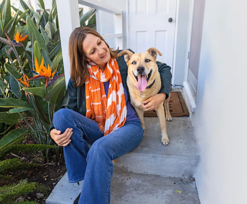 Smiling person sitting with a dog on some steps leading into a home