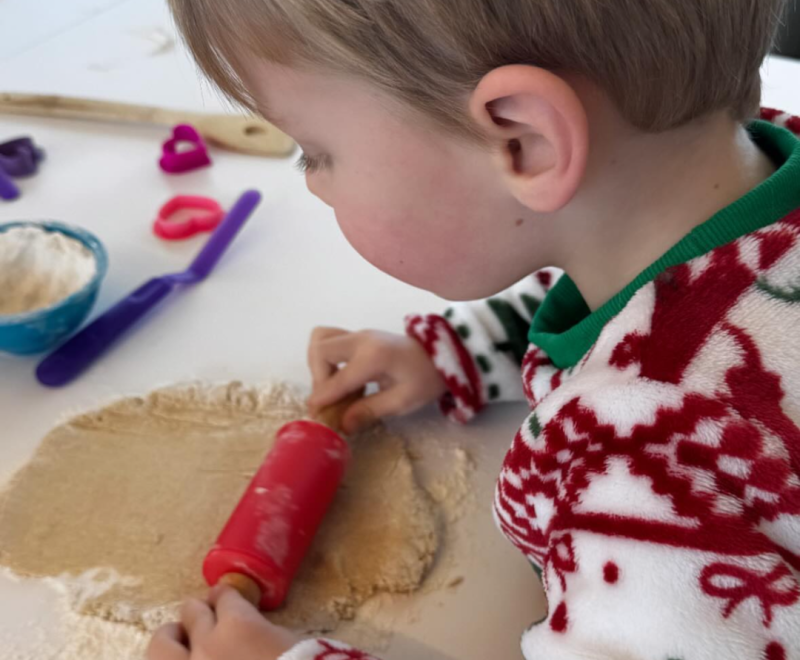 a little boy uses a red rolling pin to roll out dough for dog treats